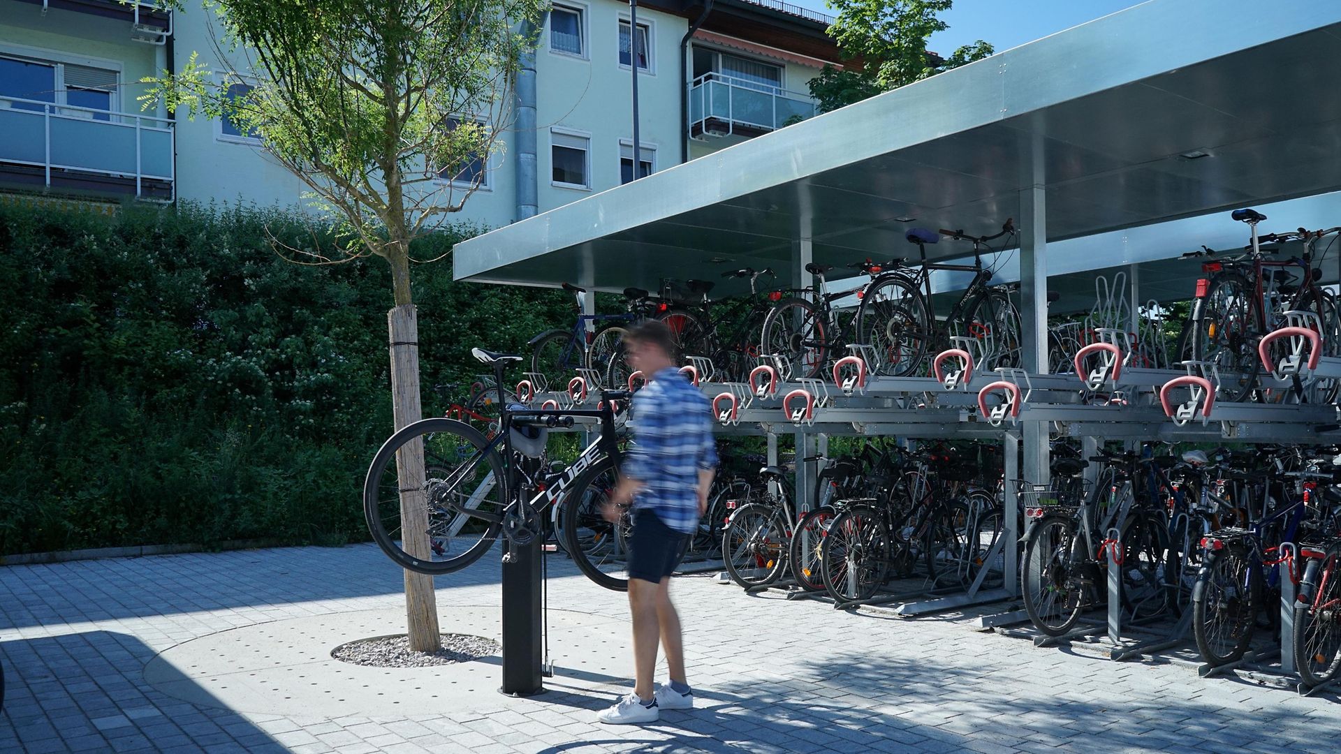 Ein Mann steht an einer Fahrradreparatursäule, im Hintergrund eine überdachte Doppelstockanlage